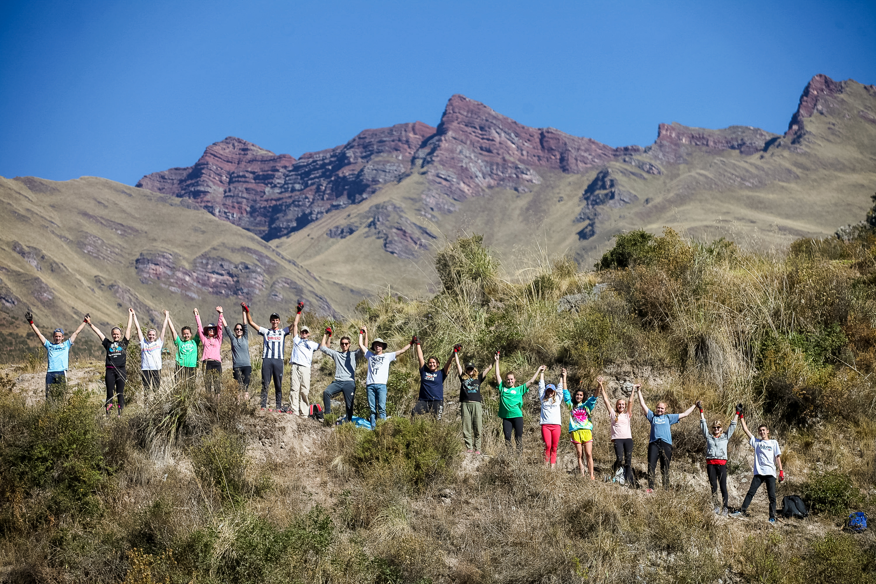 Student travelers in Peru raise their arms on a hillside beneath jagged Andean peaks