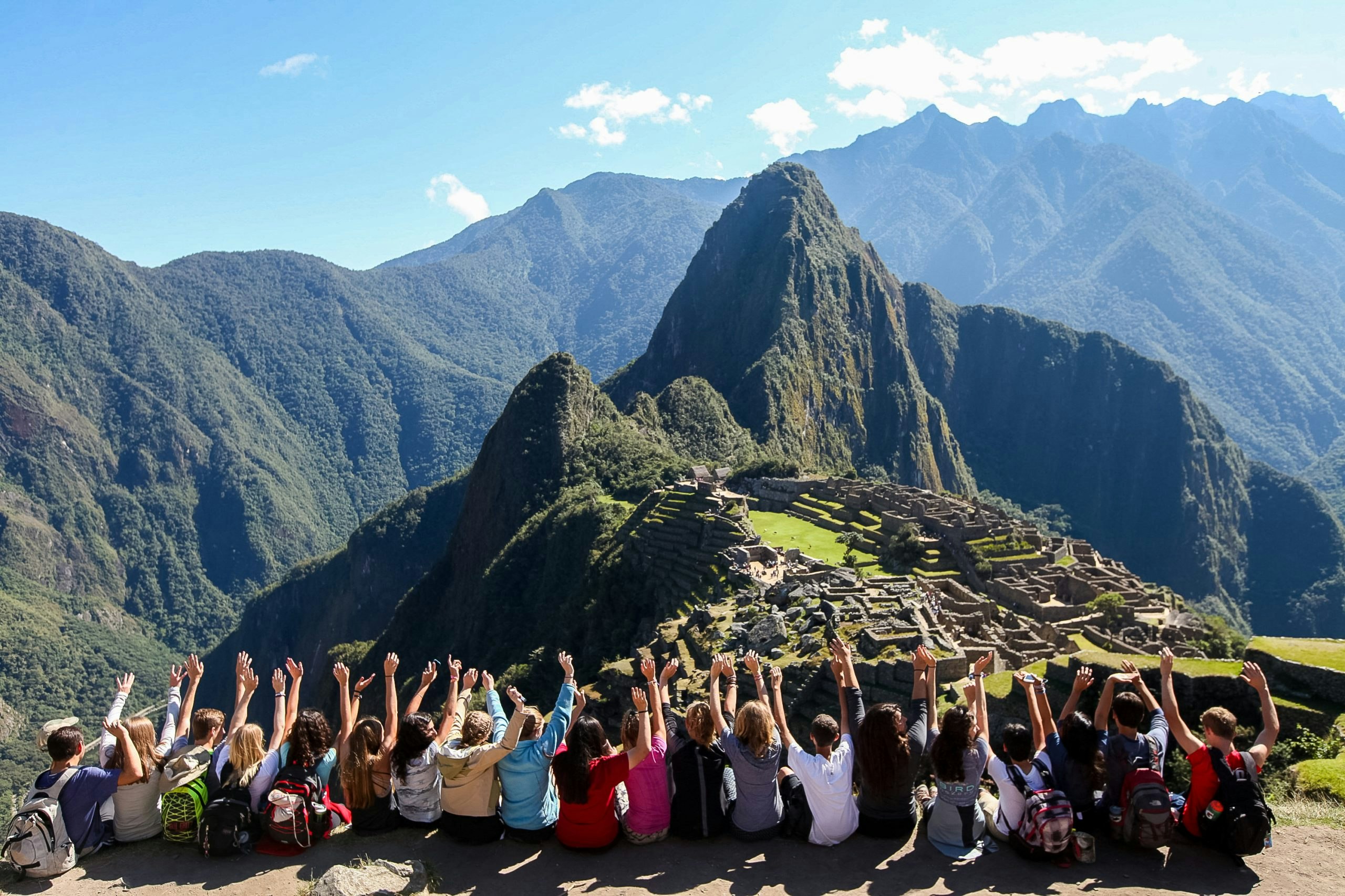 Large group of student travelers sitting and posing on a hill overlooking Machu Picchu.