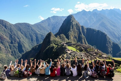 Group of student volunteers raising their hands at Machu Picchu during Summer teen tour to Peru.