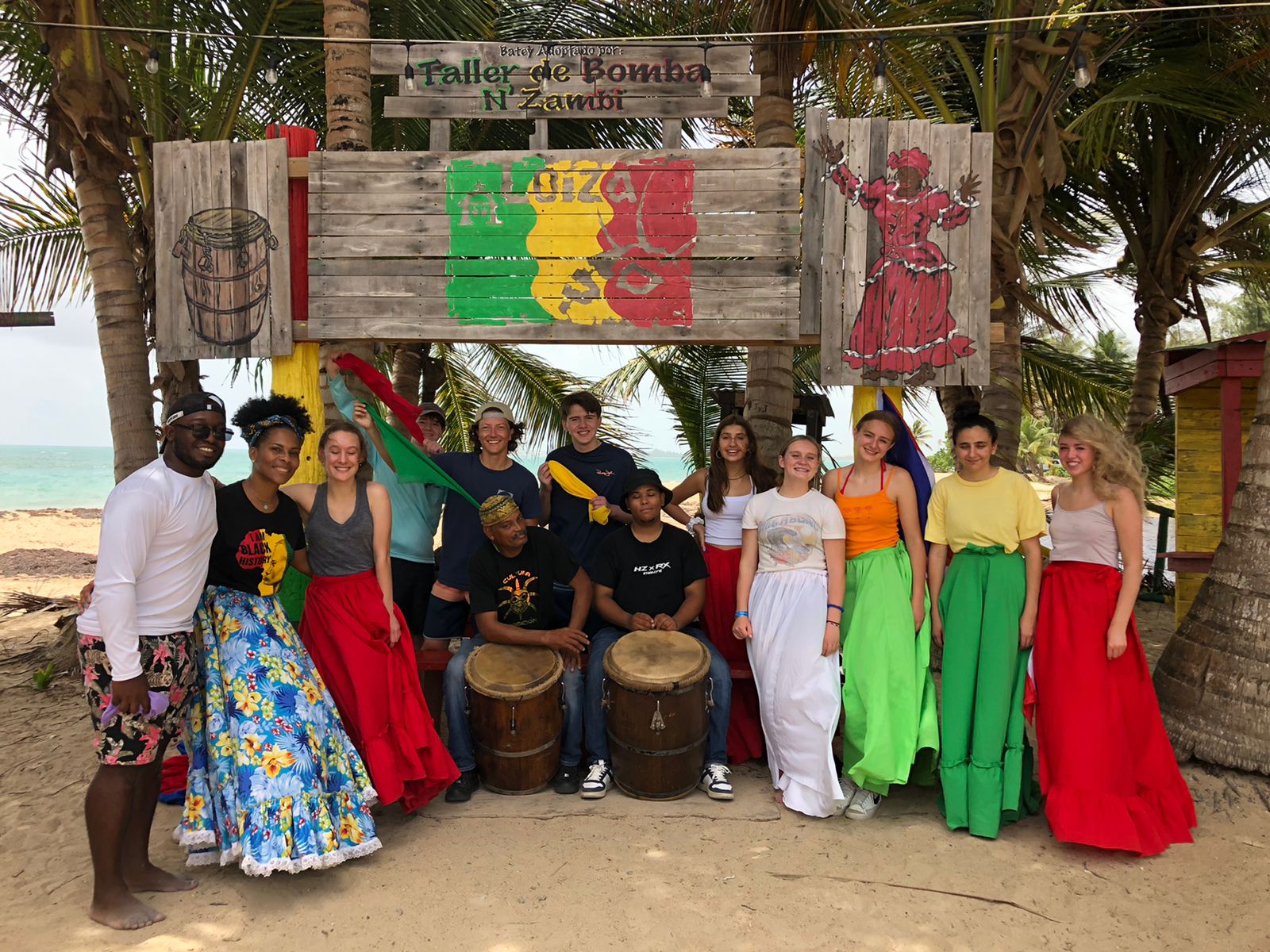 Bomba drummers and dancers in traditional dress in front of a painted backdrop.