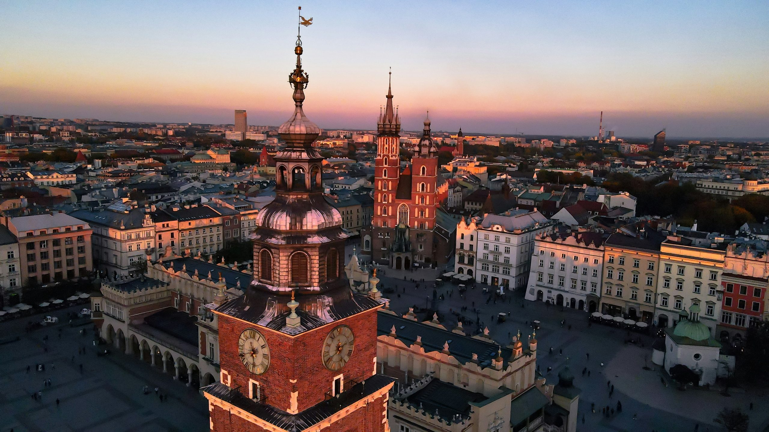 Kraków's Main Market Square at sunset, with the Town Hall Tower and St. Mary's Basilica above the rooftops.
