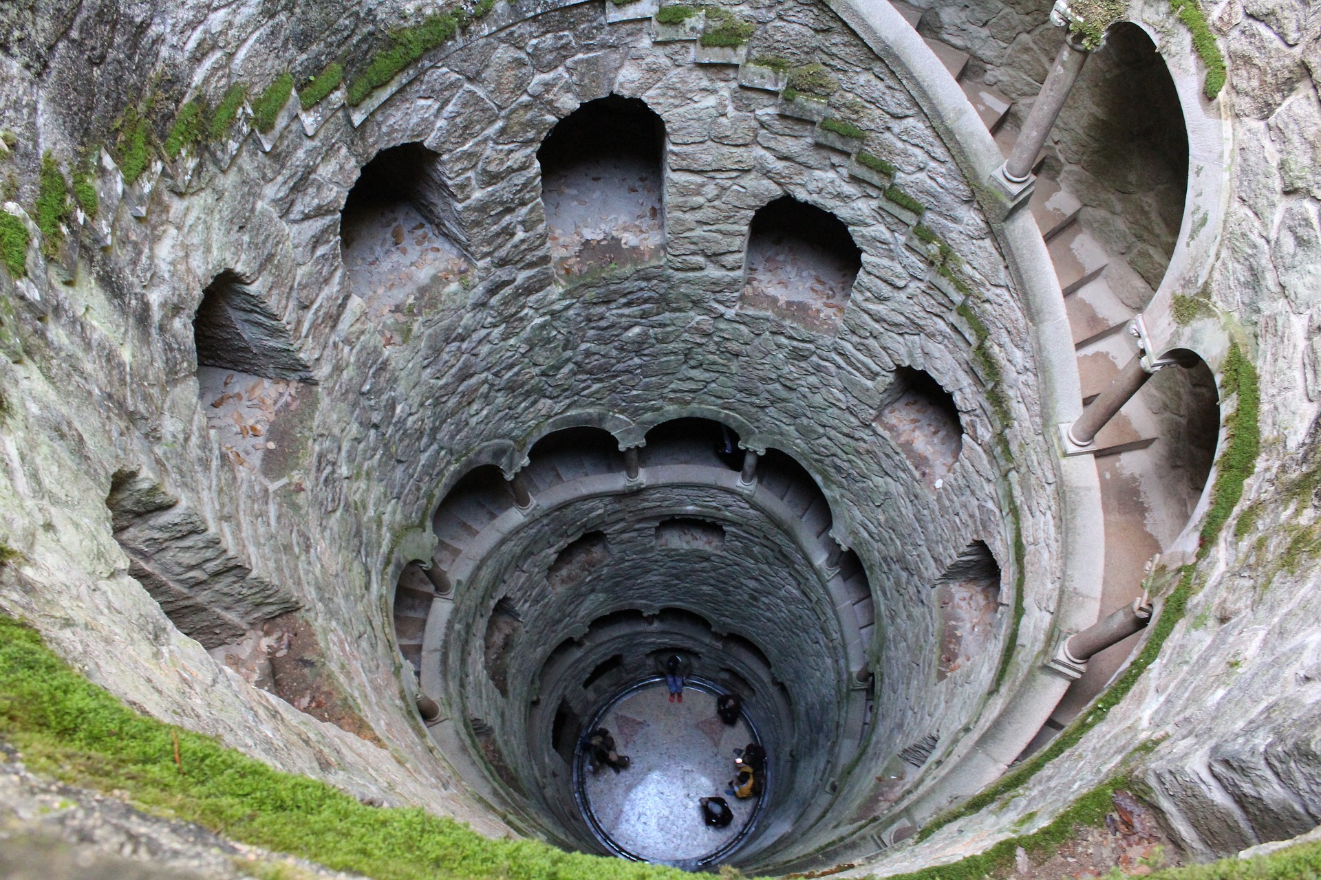 Teens descend the spiral staircase winding down the mossy stone walls of the Initiation Well in Sintra