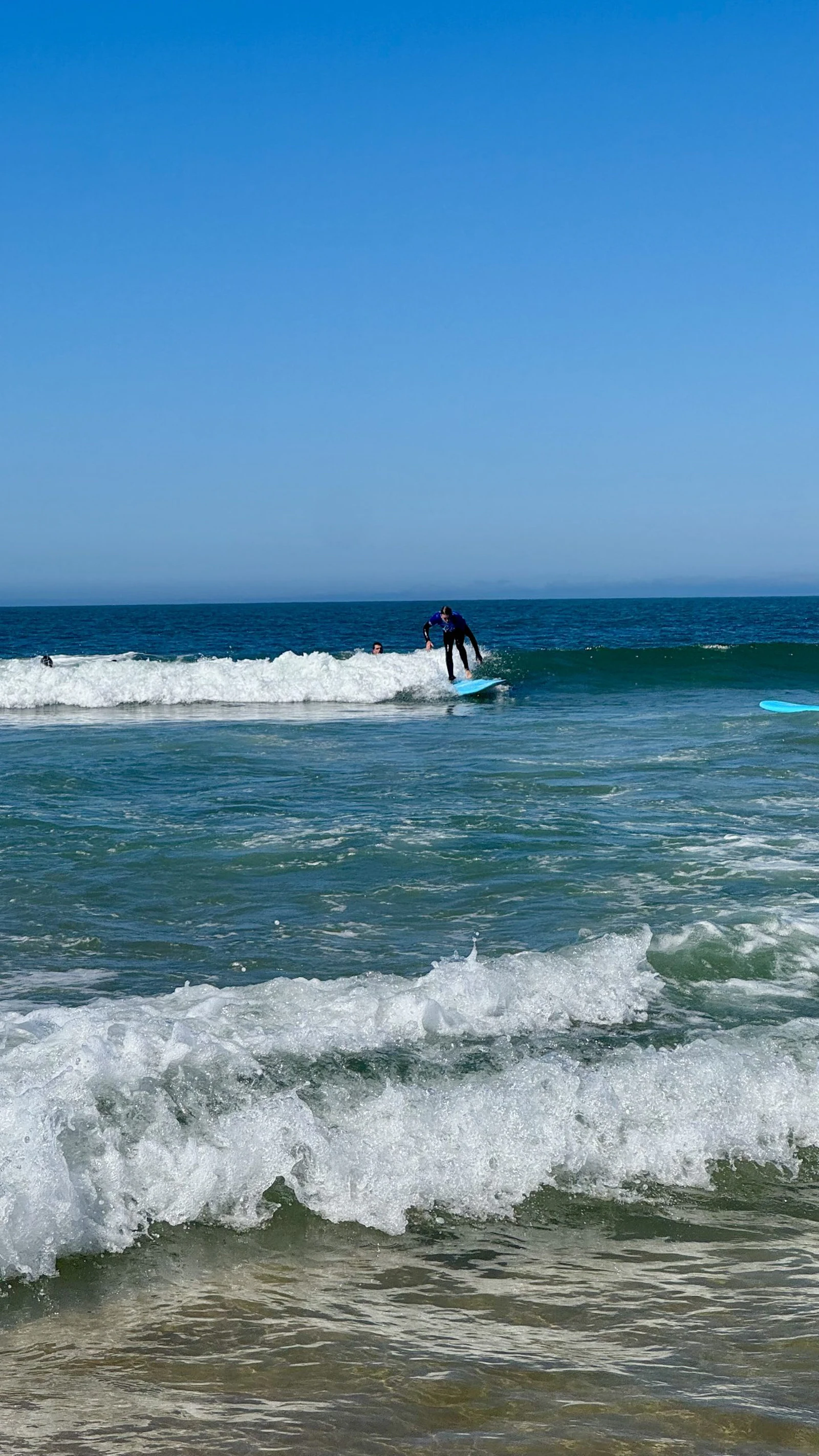 A teen traveler stands up on a surfboard riding the white water of a broken wave off a beach in Portugal