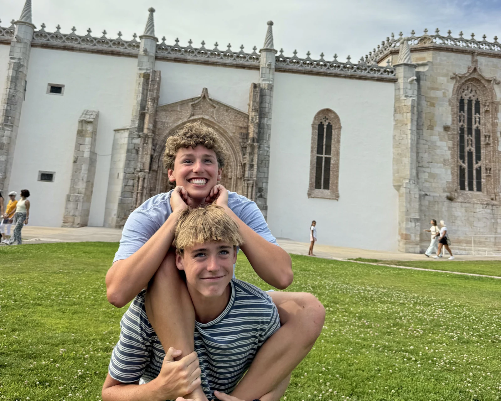 Two teen travelers clown around on the lawn in front of the white limestone walls of the Jerónimos Monastery in Lisbon, Portugal