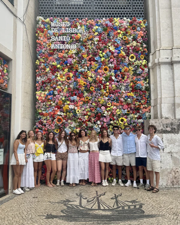 A group of teen travelers stands in front of a wall of colorful flowers at the entrance to the Museu de Lisboa in Lisbon, Portugal