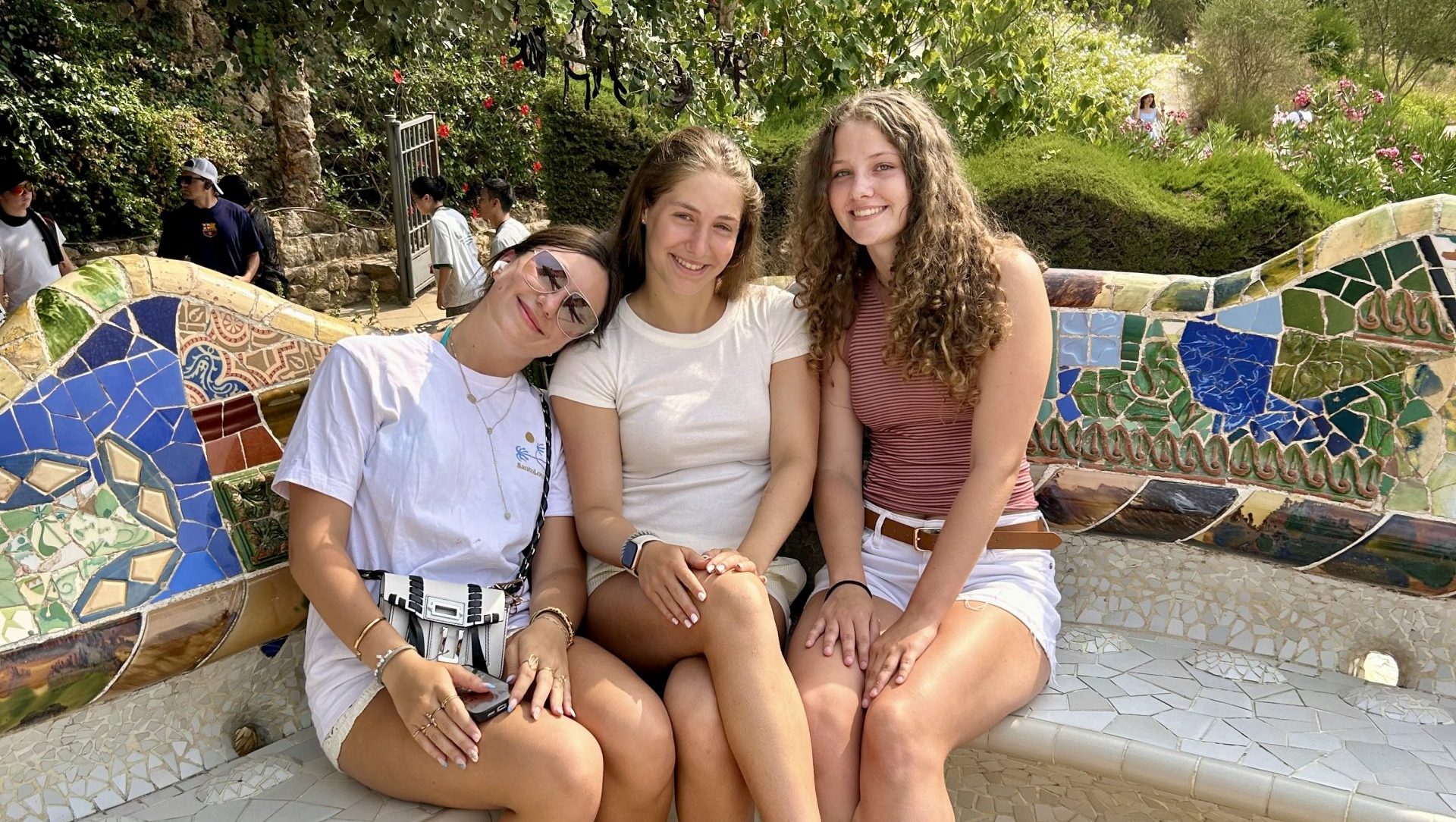 Three teen travelers sitting on a concrete bench decorated with colorful mosaic tiles.
