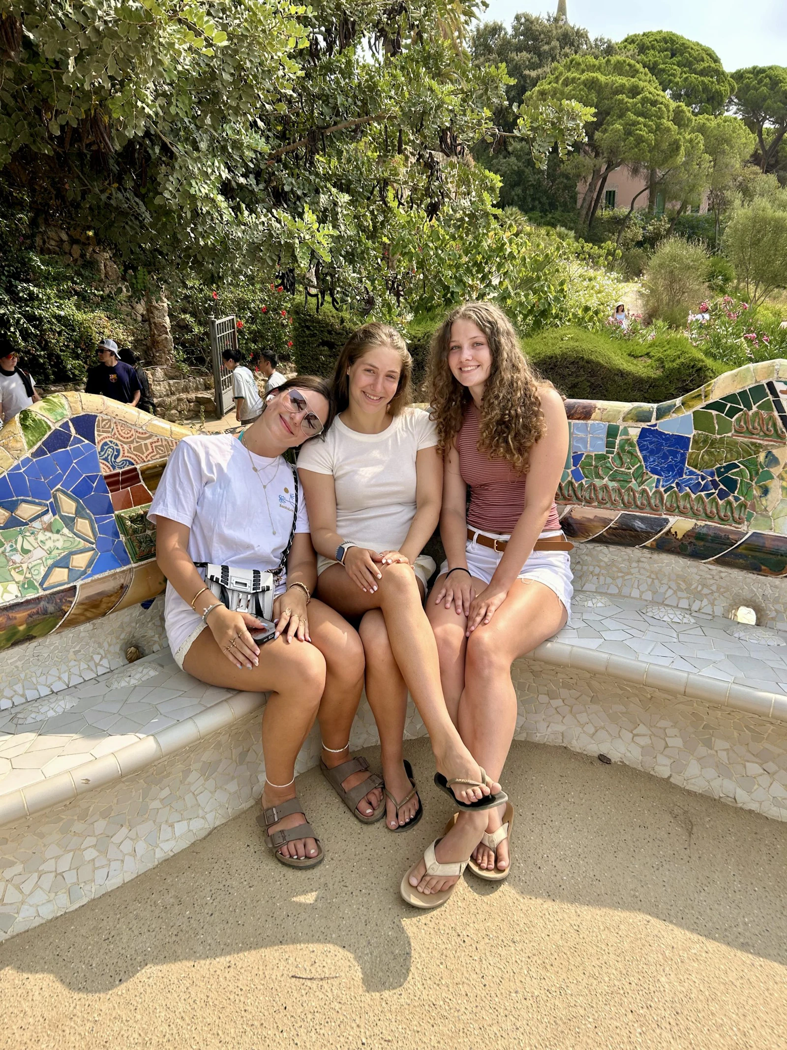 Three teen travelers sit together on the mosaic bench at Park Güell in Barcelona, Spain