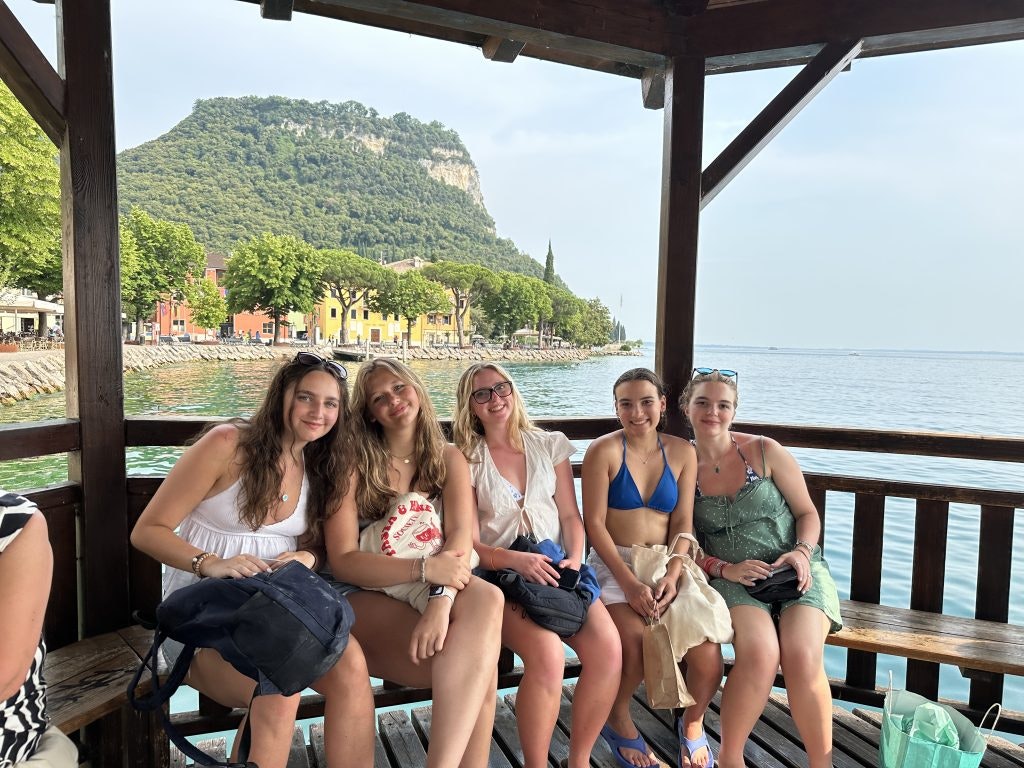 Five students sit together in a wooden gazebo by the shores of Lake Garda, with colorful houses and a lush hillside in the background--one of the best things to do in Italy.