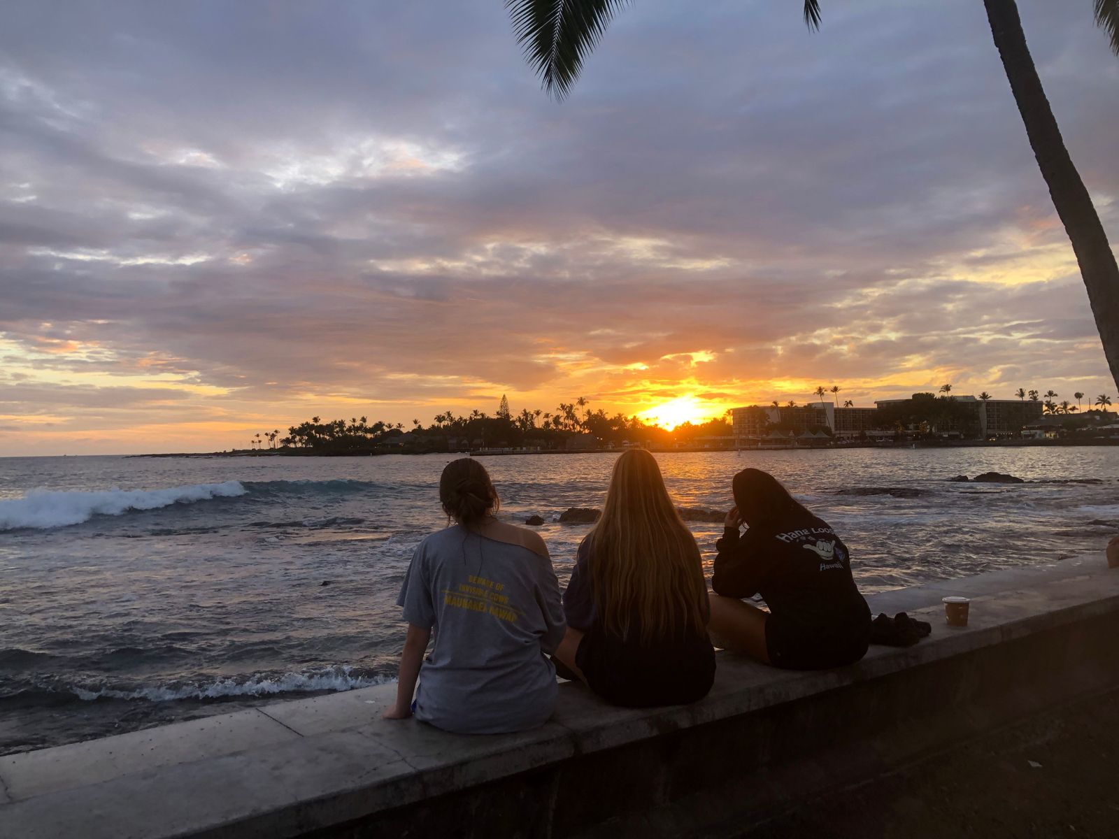 Students sit on a seawall watching the sunset over the ocean