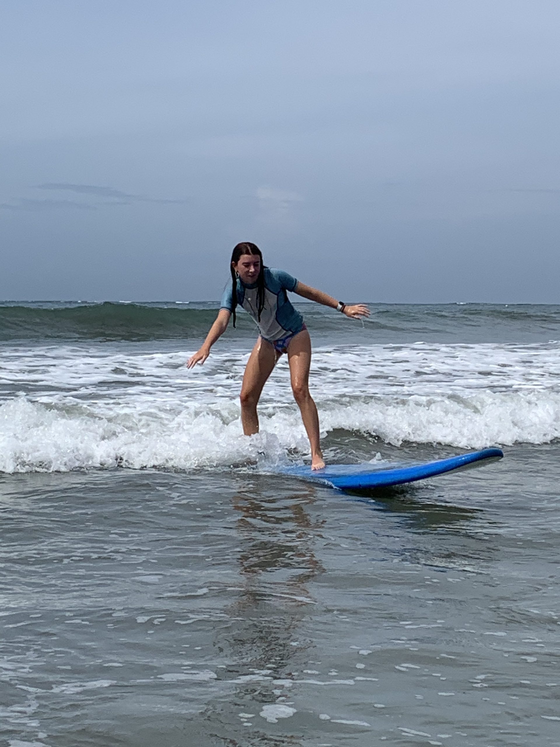 A student balances on a surfboard as it glides through the whitewash