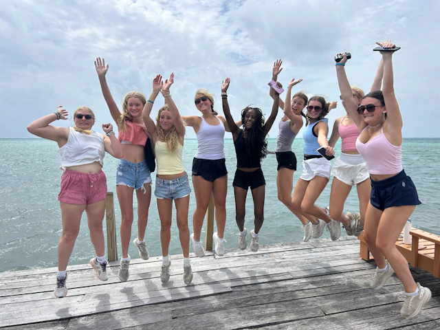 A group of Rustic Pathways students jump and cheer on a wooden dock over the Caribbean Sea in Belize