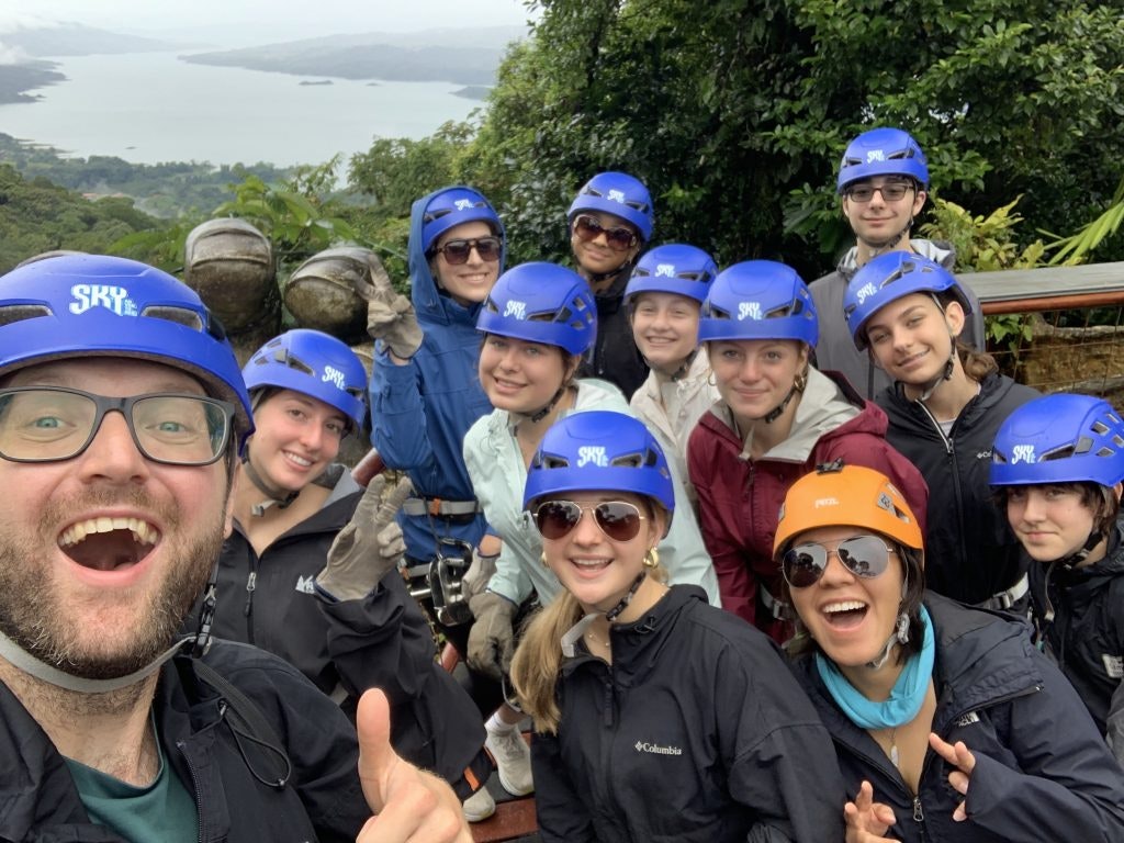A group of student travelers and a chaperone in hard hats and safety gear during an activity on a Rustic Pathways trip.