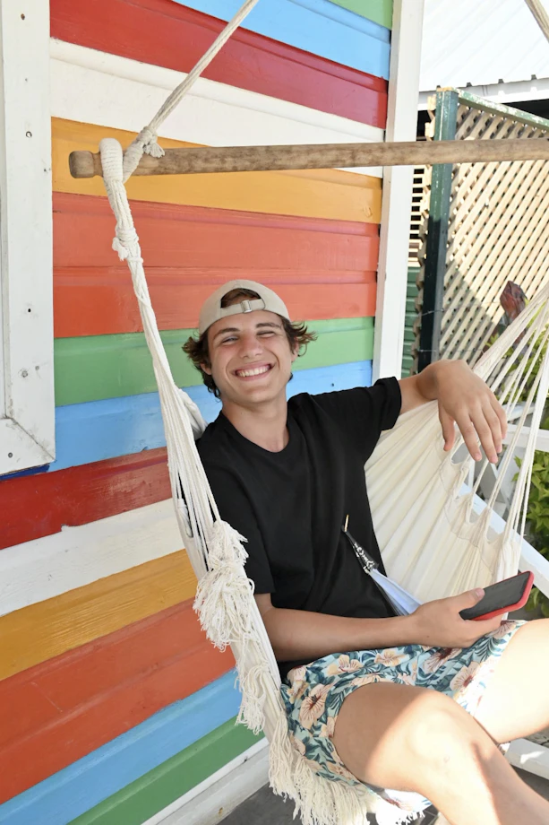 A smiling teen traveler relaxes in a hammock beside a rainbow-painted wall in the Dominican Republic