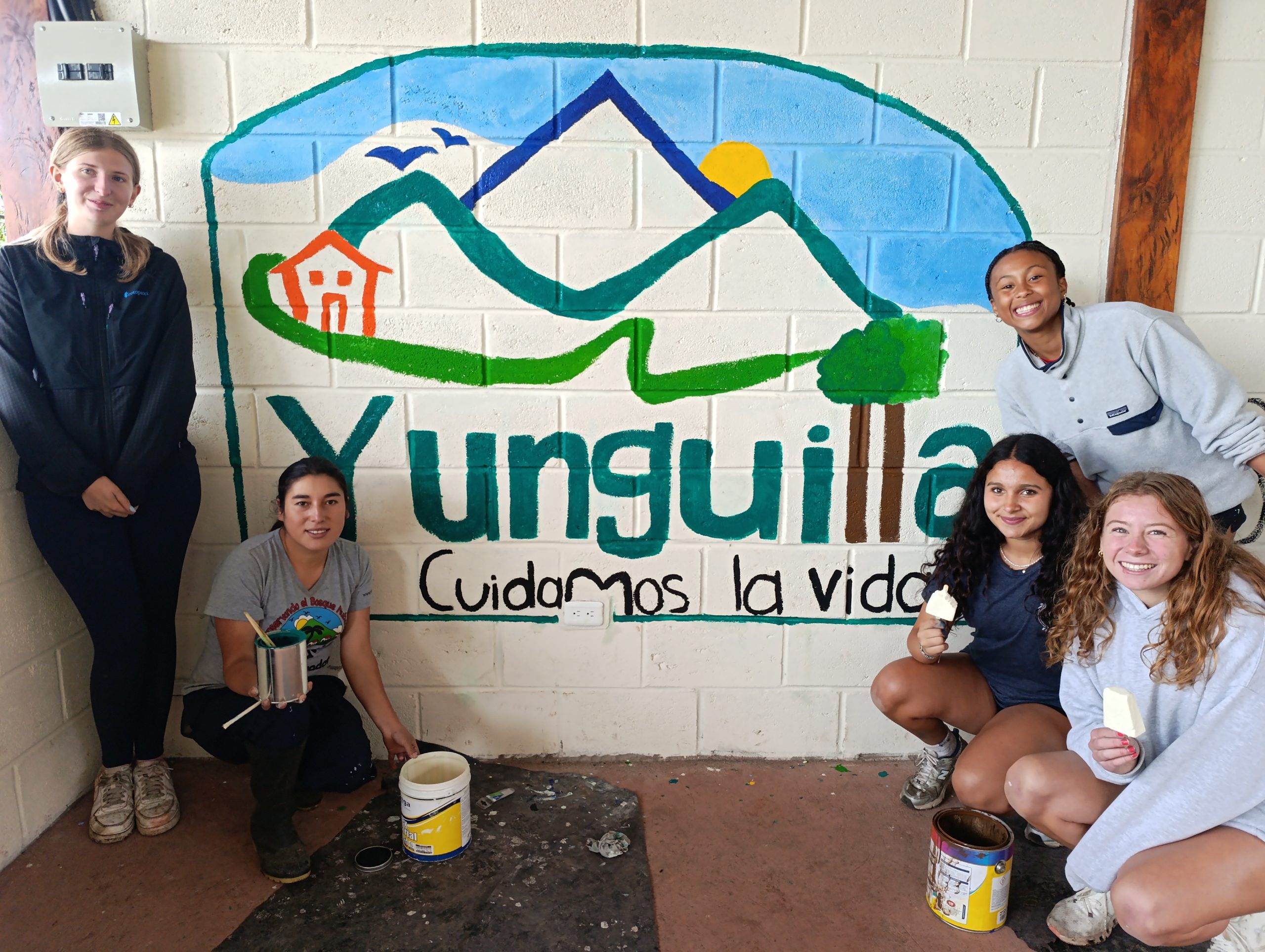 Student travelers pose beside a painted mural reading Yunguilla, Cuidamos la vida