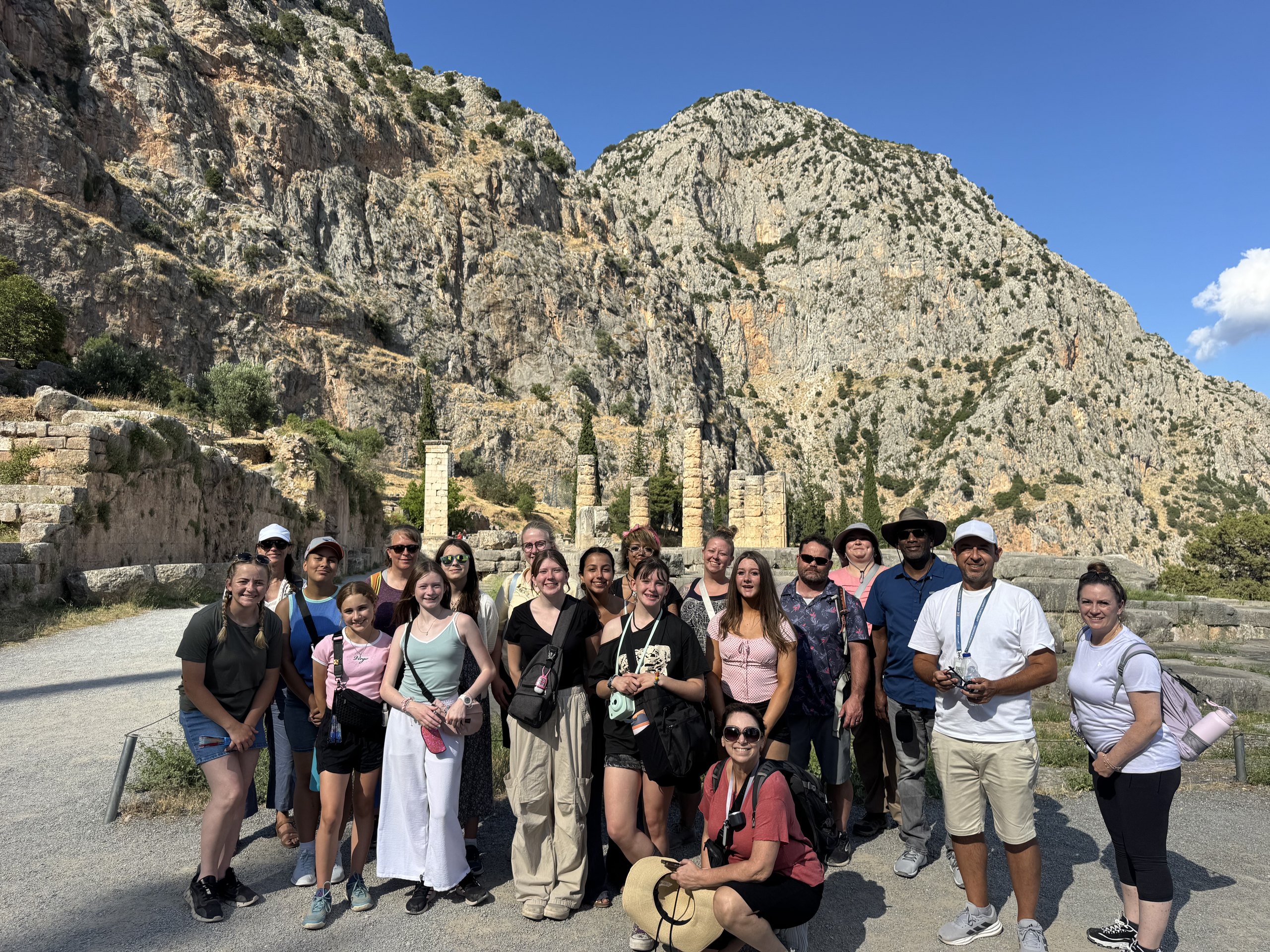 A school group with their teachers at the sanctuary of Delphi, the columns of the Temple of Apollo and the cliffs of Parnassus behind them.