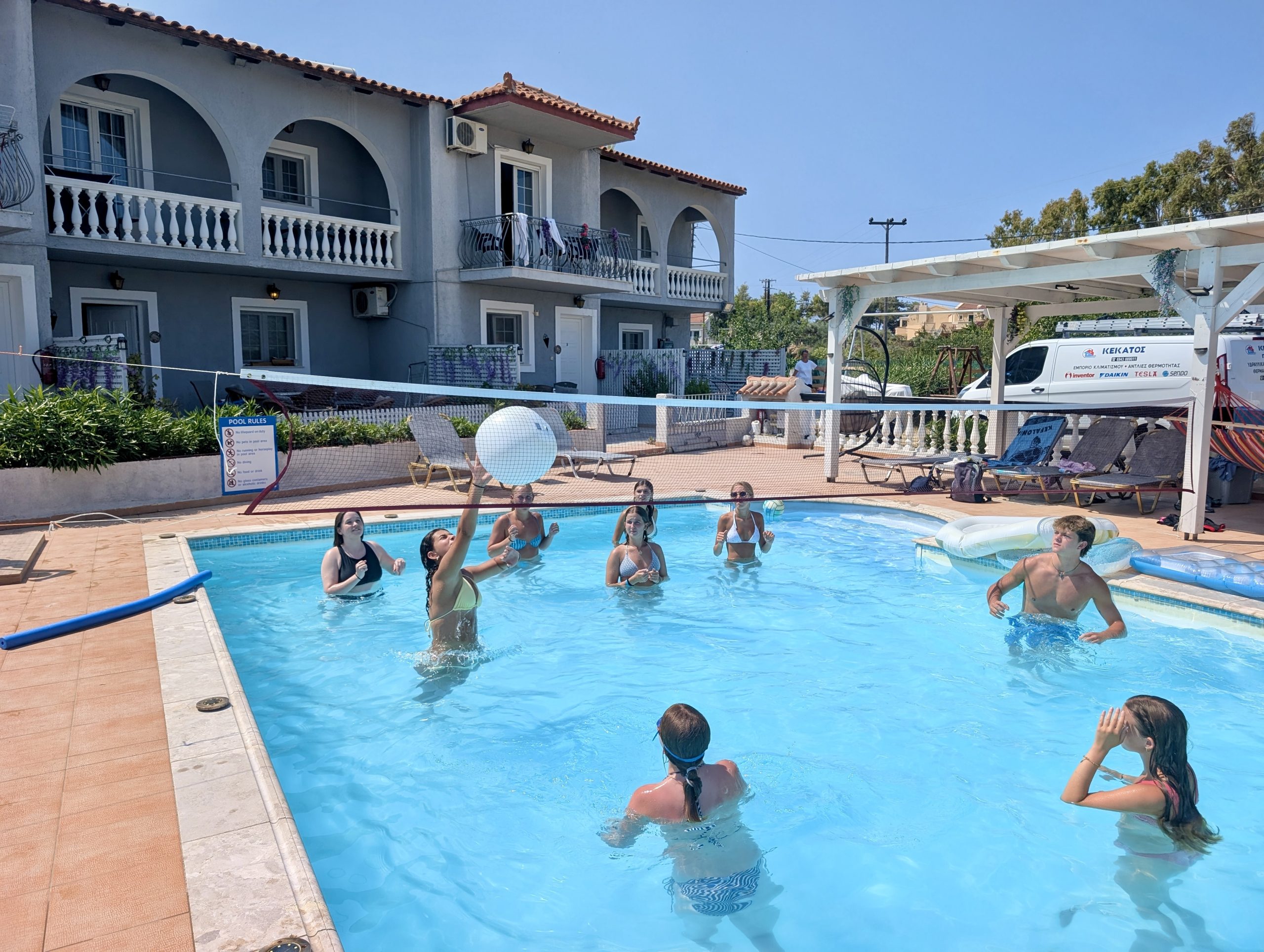 Teens play volleyball in a pool beside a Greek villa