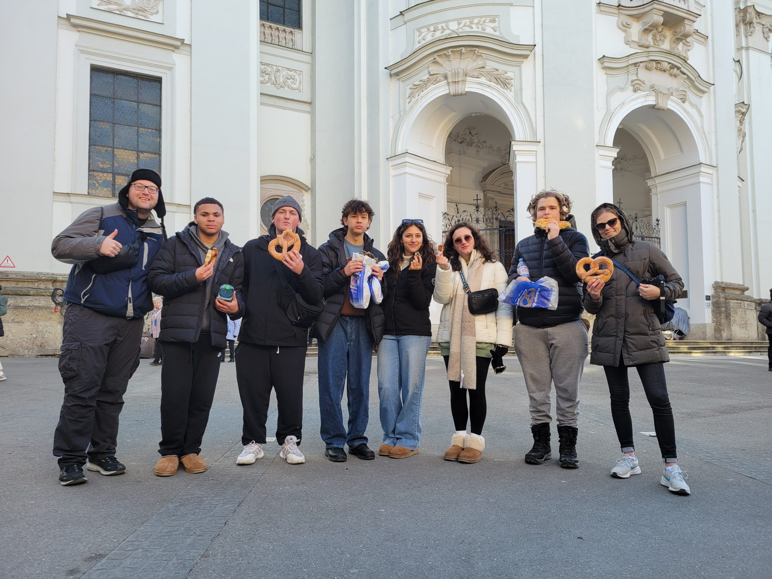 Group of teen travelers enjoying traditional German pretzels in front of a historic church, part of a Rustic Pathways student travel experience in Germany.