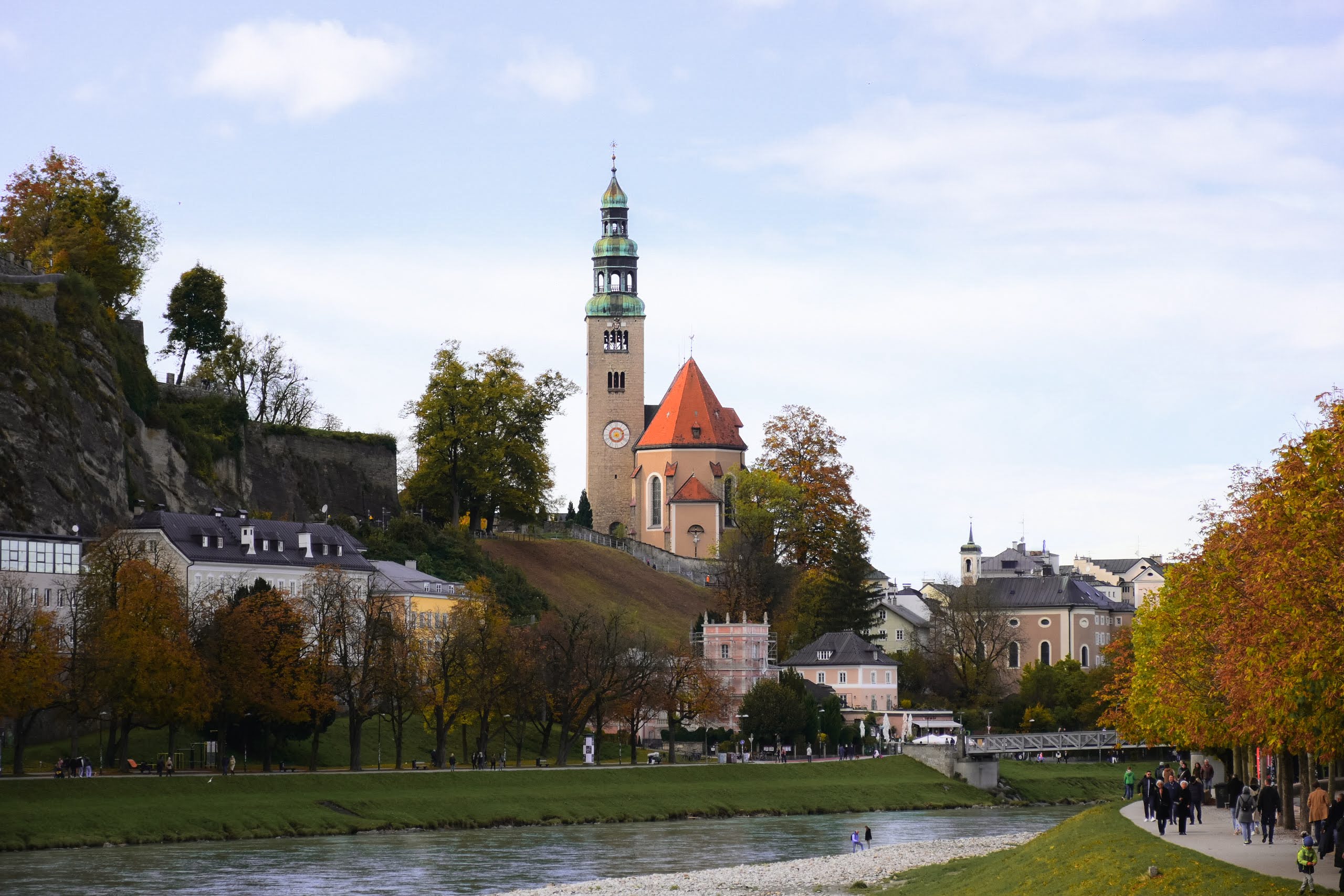 A church with a red roof on a hill, next to a river.