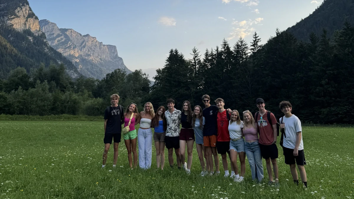 A group of teen travelers stands in an alpine meadow below steep mountains in Germany