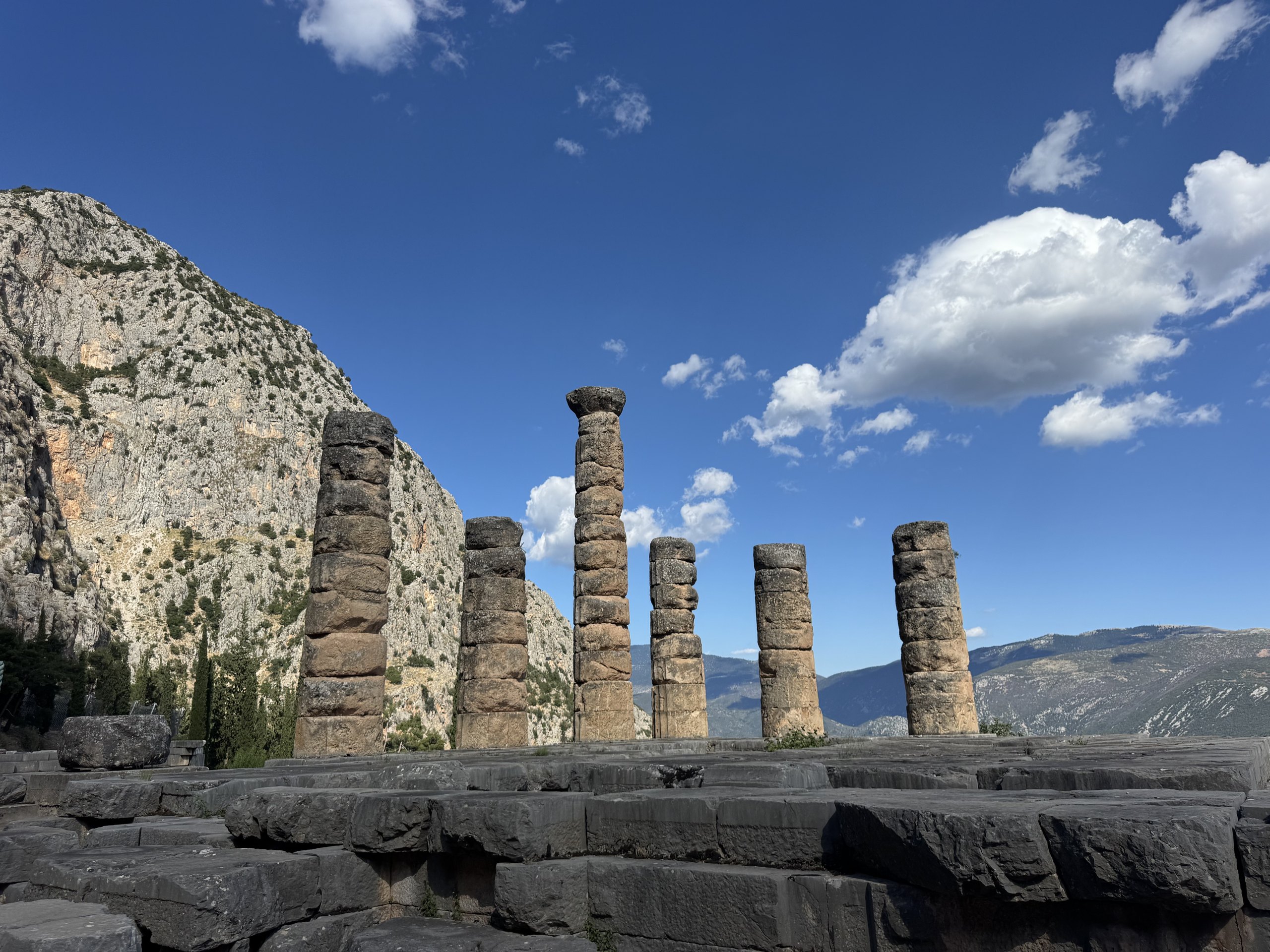 Six standing columns of the Temple of Apollo at Delphi on their stone platform, below the Phaedriades cliffs.