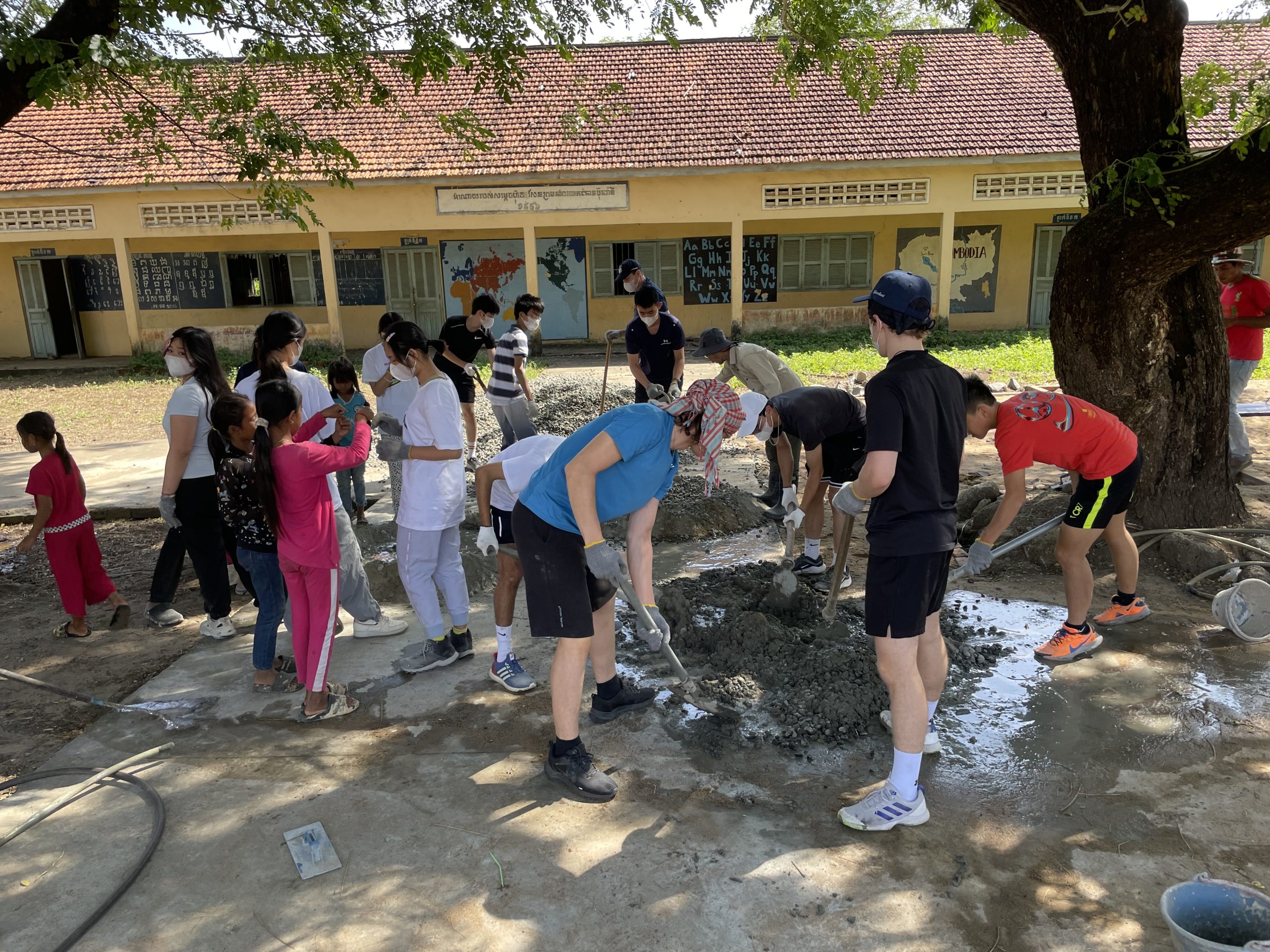 Students mix concrete outside a village school building in Cambodia