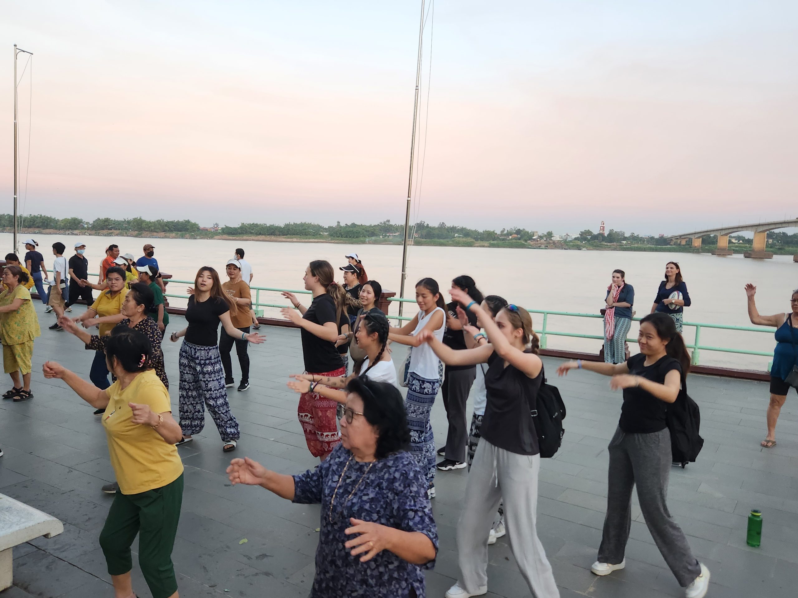 Students join a group aerobics session along a riverside promenade at dusk