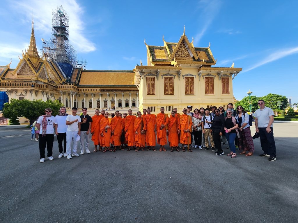 Group of tourists and monks posing in front of a Cambodian temple.
