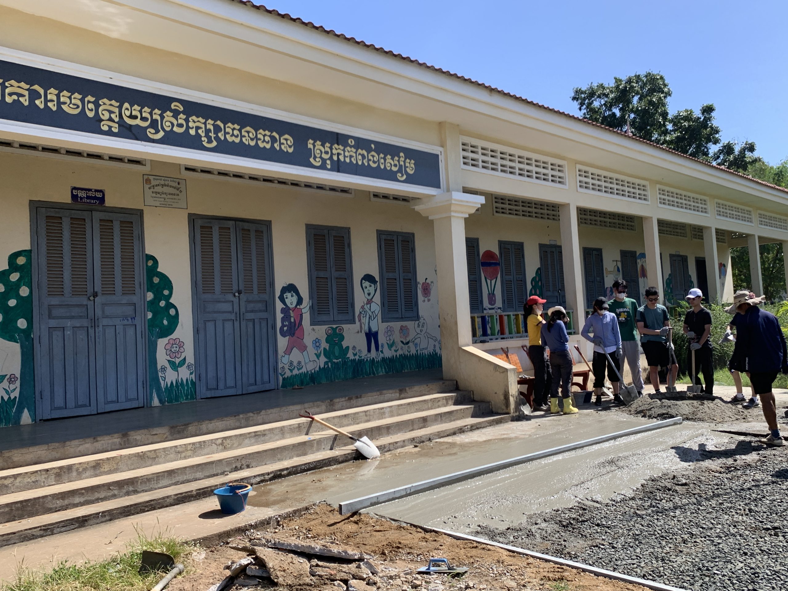 Students mix concrete outside a painted schoolhouse in Cambodia
