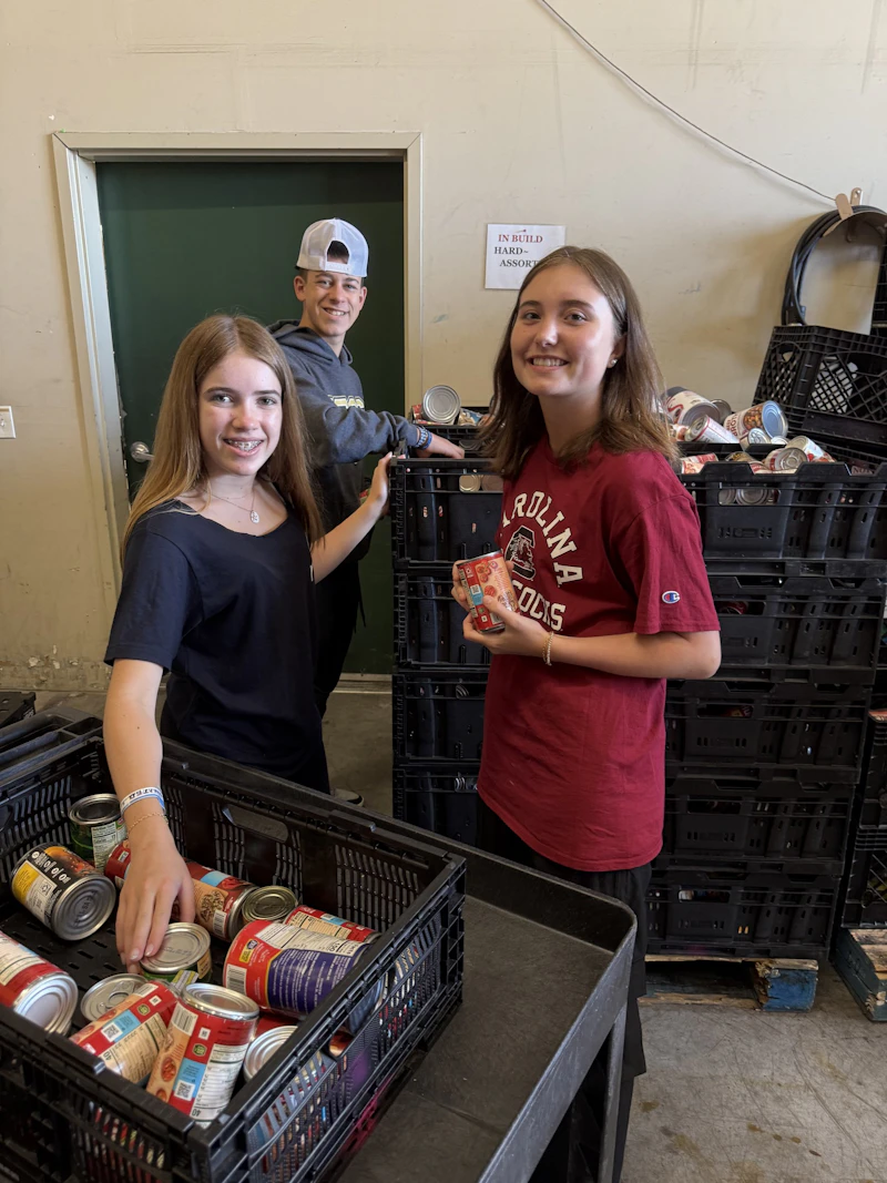 Two teen travelers smile while sorting canned food into crates at the Kona Food Bank in Hawaii