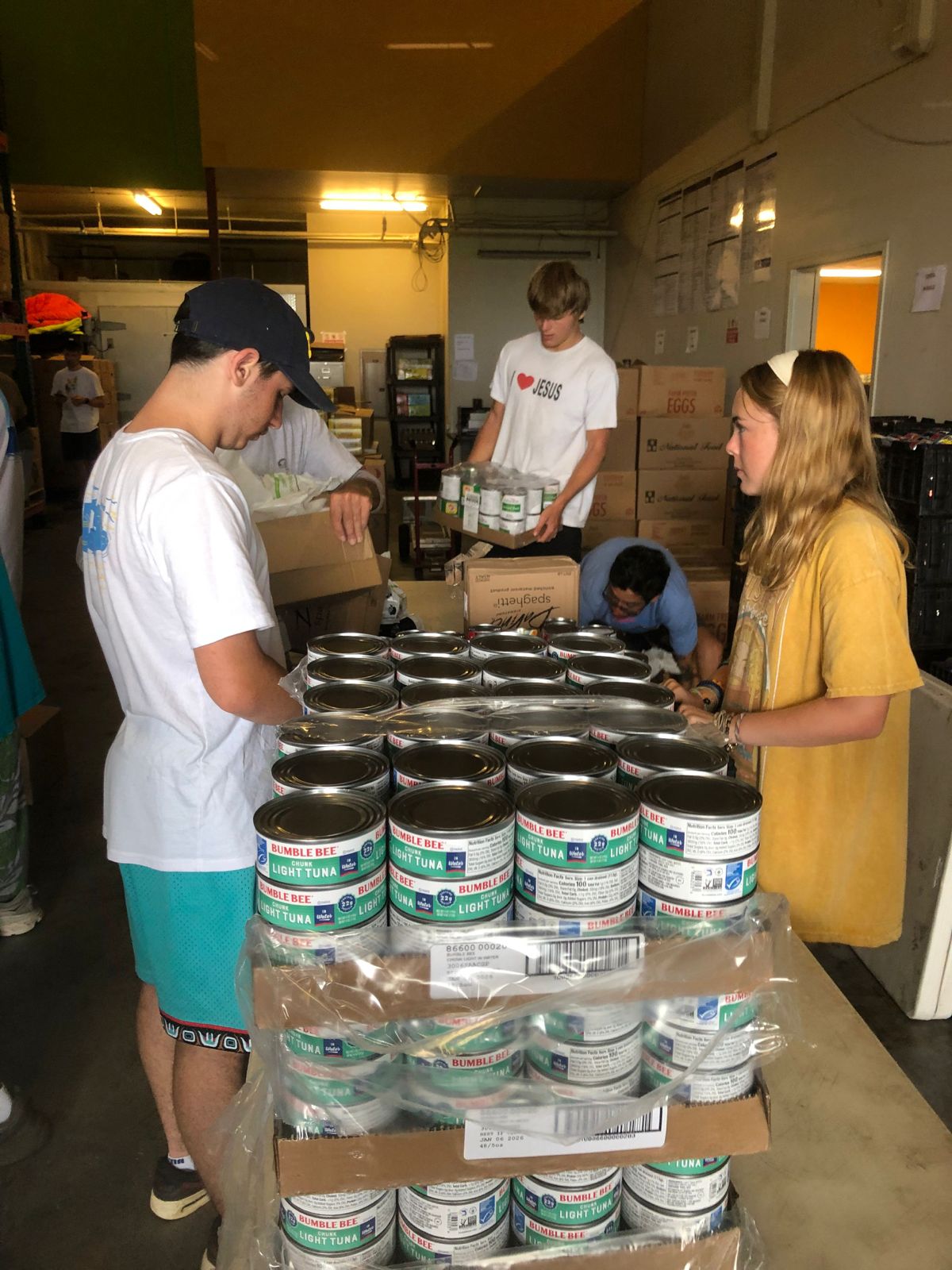 Students sort canned tuna into stacks at a food pantry warehouse