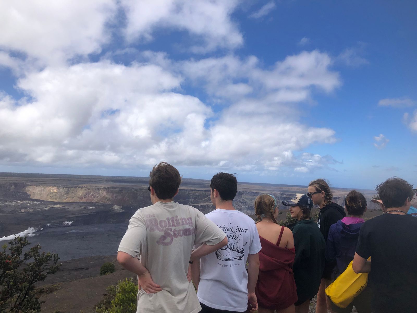 Students look out over a volcanic crater under a partly cloudy sky