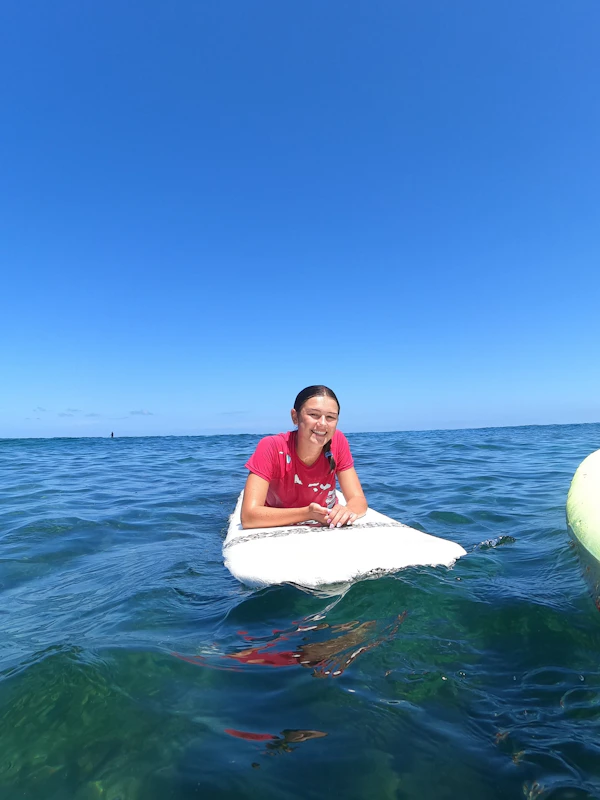 A teen traveler smiles while lying on a surfboard in clear blue water off Hawaii