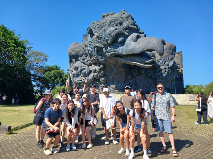 A group of students stands in front of a giant carved stone bird head at a cultural park in Bali