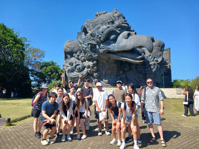 A group of students stands in front of a giant carved stone bird head at a cultural park in Bali