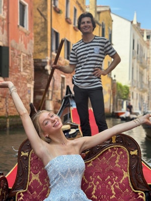 A female student smiles with her hands raised as she enjoys a gondola ride during an Italy teen tour