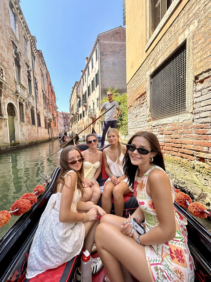 Teen travelers take a selfie on a gondola in a narrow Venice canal