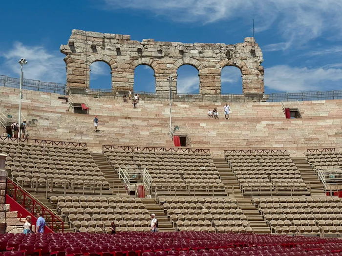 Tiers of weathered stone seating rise inside a Roman amphitheater, with arched openings cut through the outer wall.