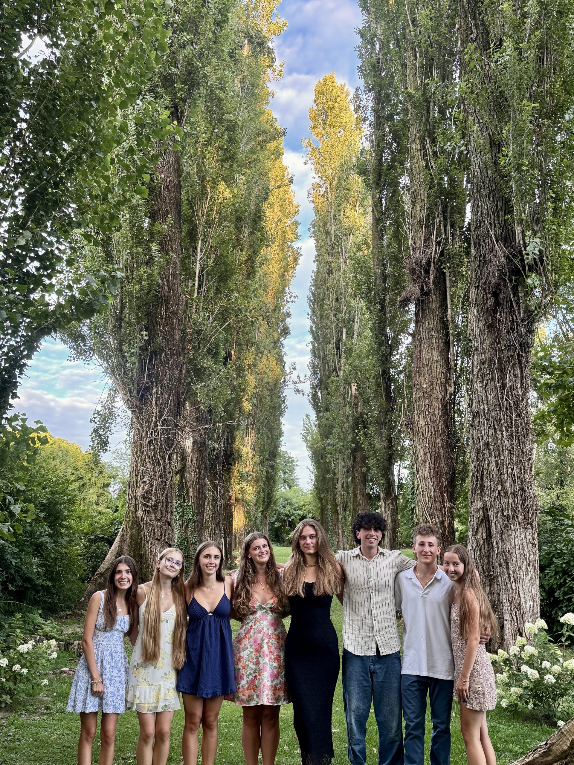 Students pose together beneath a row of tall poplar trees