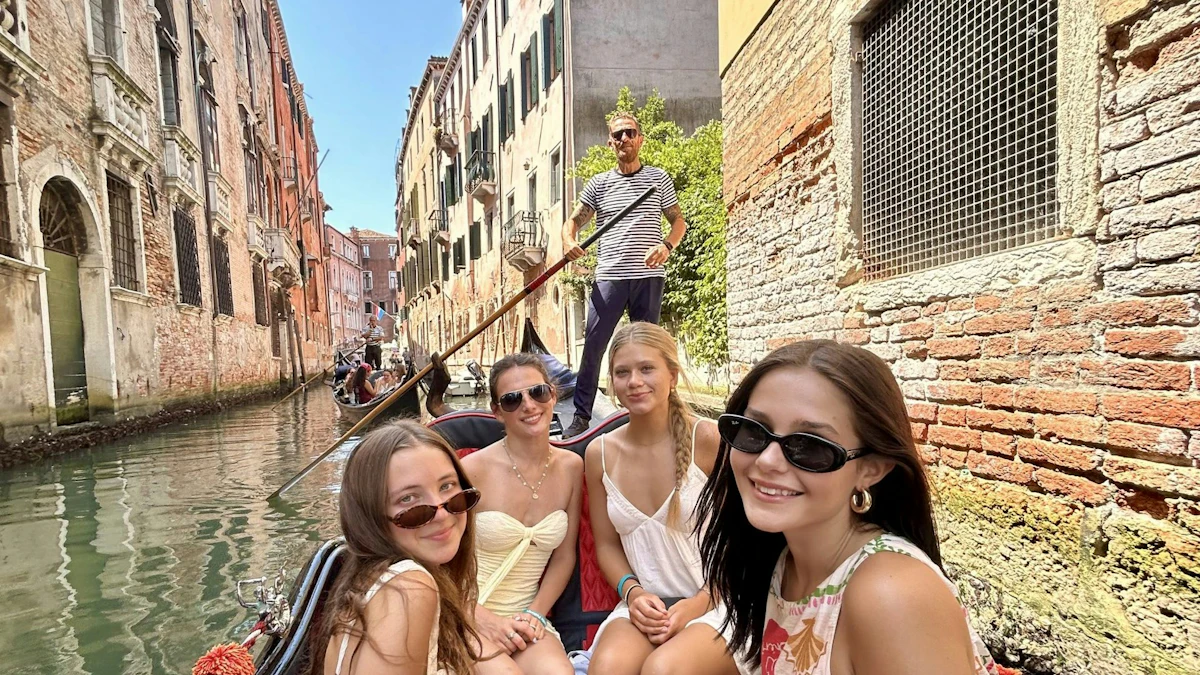 Teen travelers take a selfie on a gondola in a narrow Venice canal