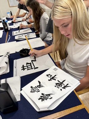 A student practices drawing Japanese characters in ink during a teen tour in Japan