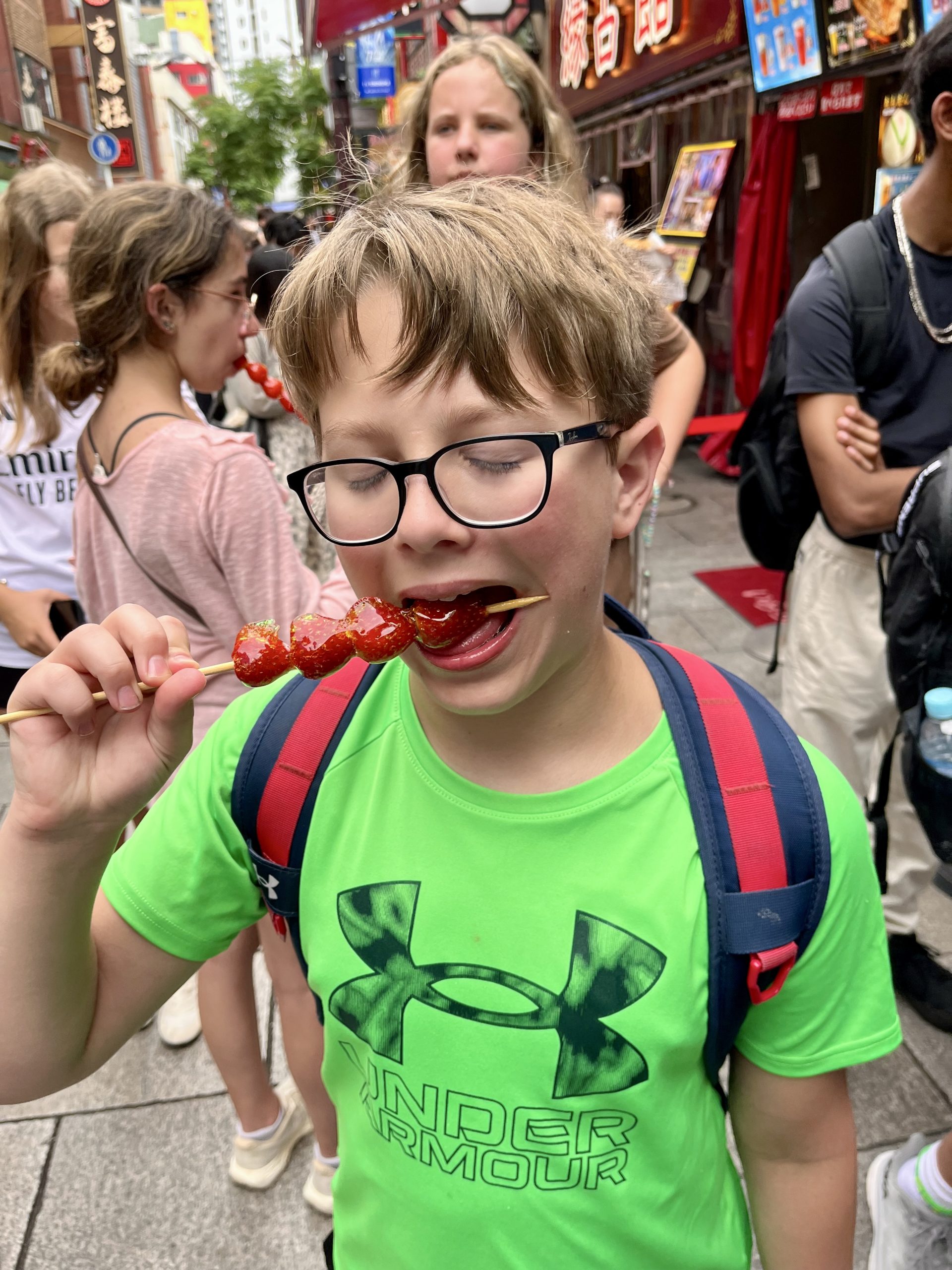 A student bites a candied fruit skewer on a busy Tokyo street