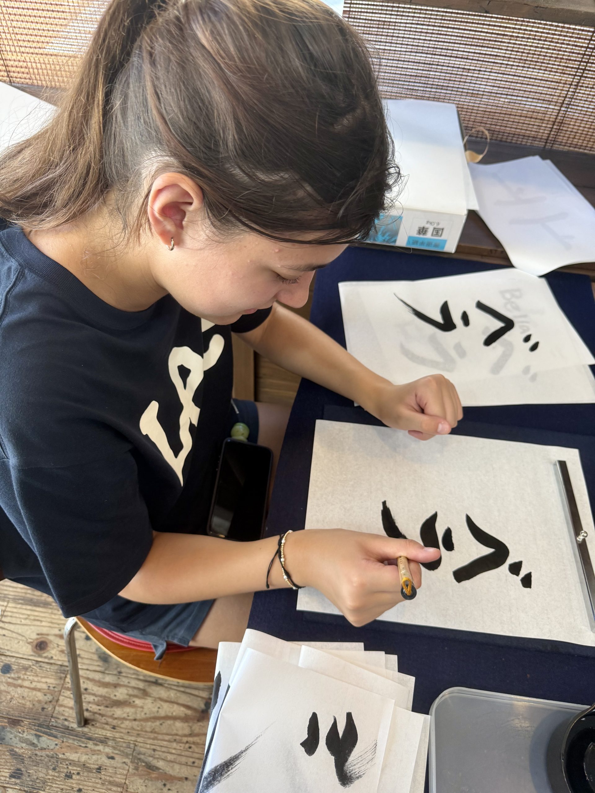 A student practices Japanese calligraphy strokes with a brush on rice paper