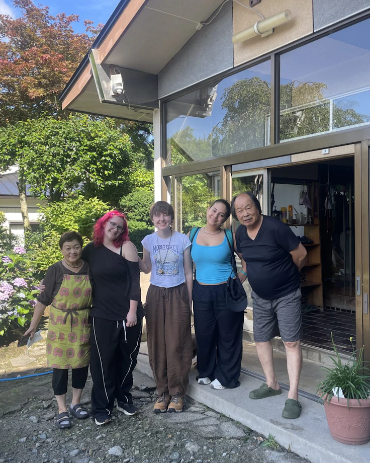 Teen travelers stand with their homestay host family outside a house with hydrangeas in Japan