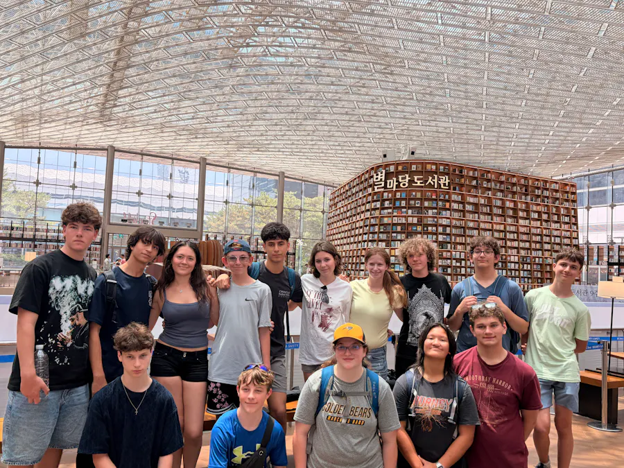 A group of teenage students standing together in front of the tiered bookshelves of a large indoor library atrium in Seoul