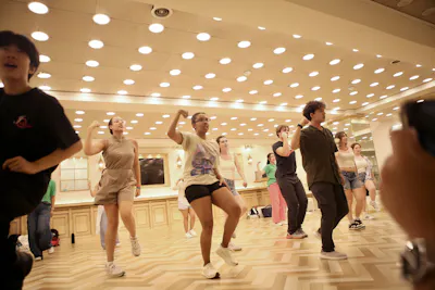 Students mid-step in a mirrored studio during a K-pop dance class, an instructor leading from the front