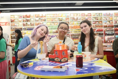 Three teen travelers eating instant noodles at a table inside a brightly lit snack shop during a teen tour in South Korea.