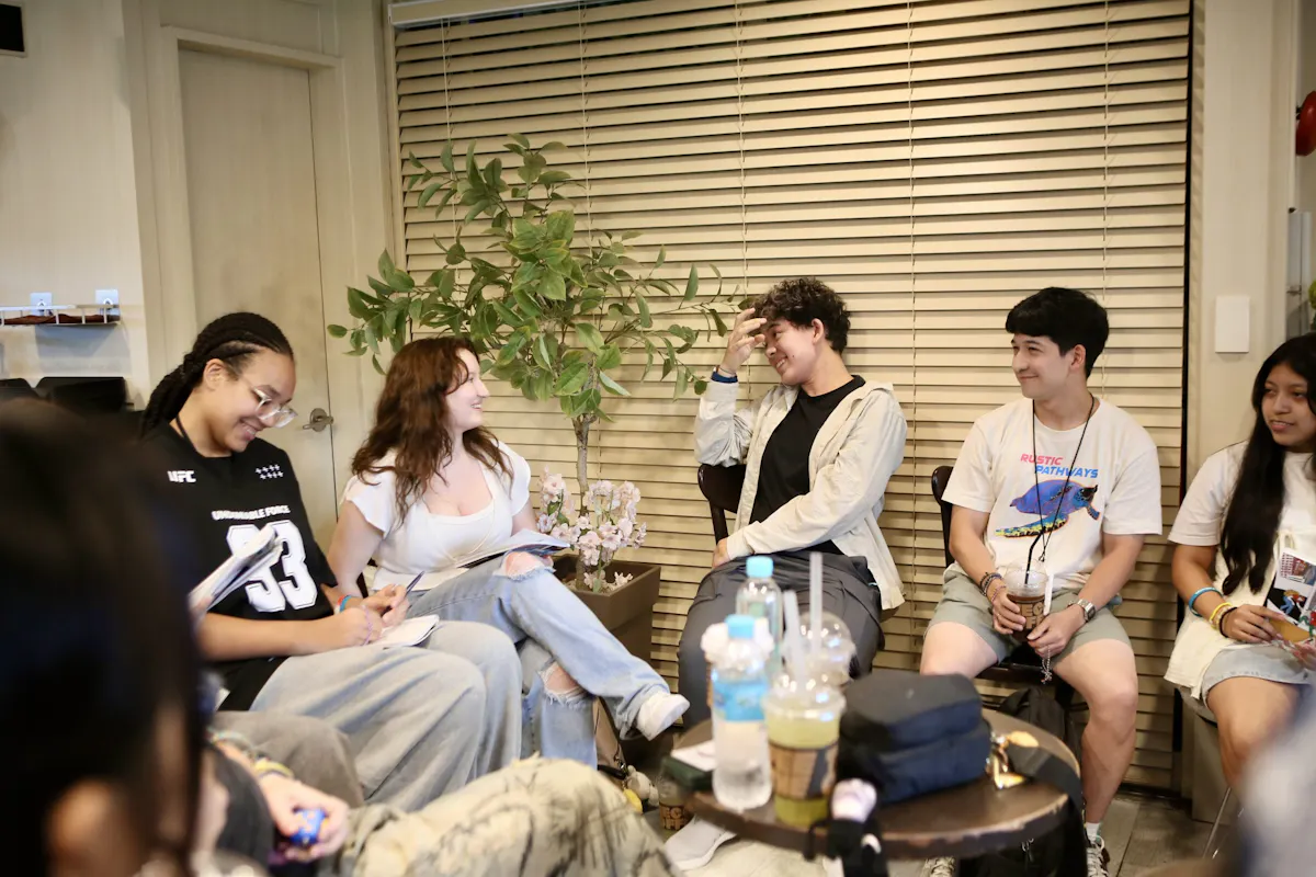 Students sitting together on low chairs in a cafe, talking and laughing over drinks