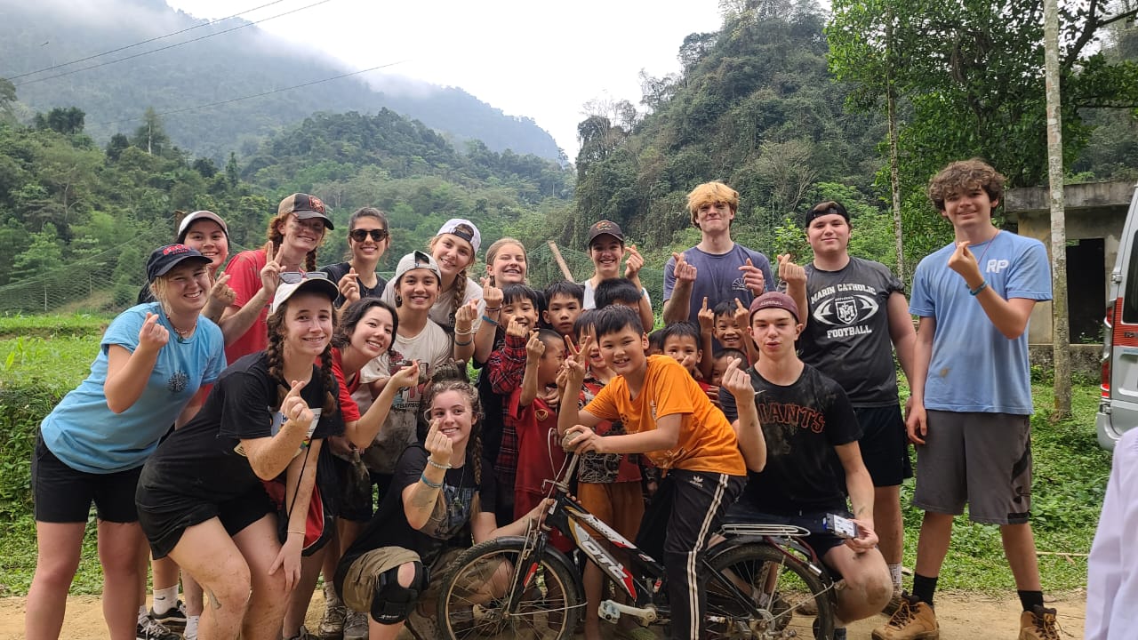 Group of cheerful volunteers and local children posing together in a mountainous area of Vietnam.