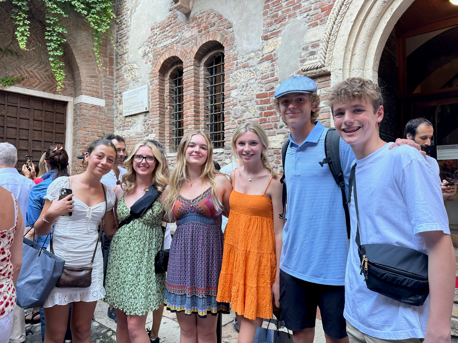 Six teen travelers in summer clothes stand together in a busy stone courtyard in Italy