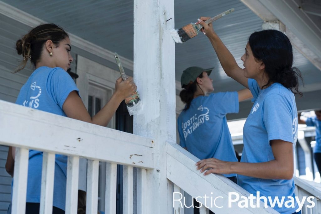 High school students painting the columns of a porch as part of a service learning project in New Orleans.